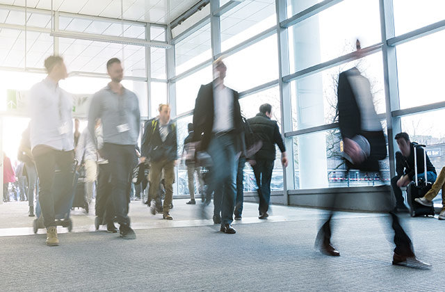 Menschen in Businesskleidung gehen in einem hellen, modernen Gebäude mit großen Fenstern und Teppichboden